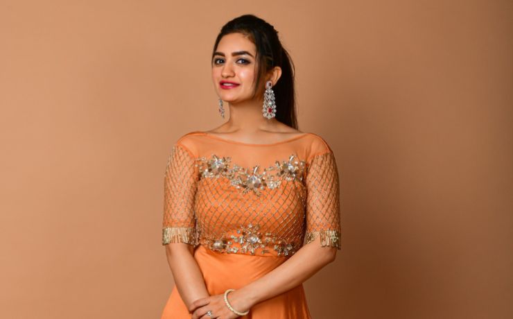 A young girl in an orange satin gown with gold work standing in a studio.